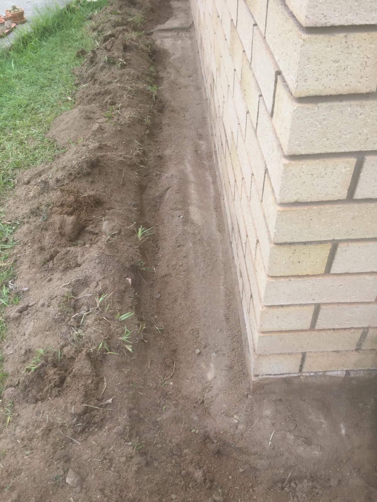A trench dug along a brick house foundation